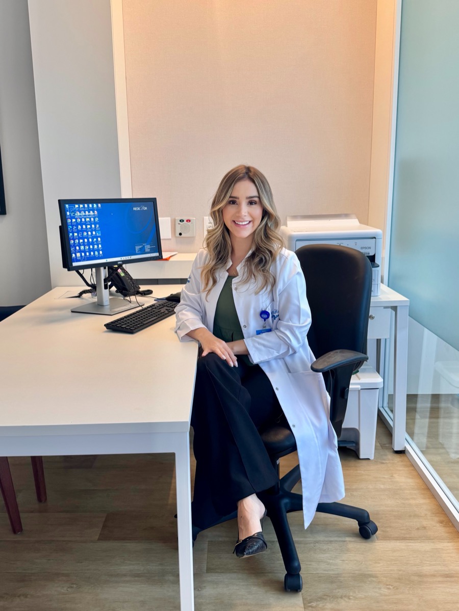 Dra. Yasmin Miglio sentada em seu consultório, ao lado da mesa de atendimento.